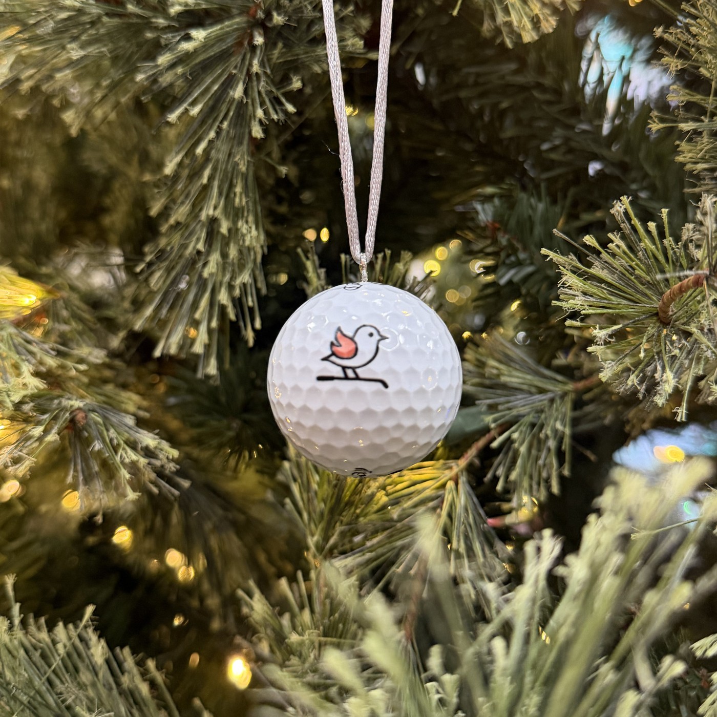 Hot Birdie golf ball ornament with silver ribbon beside candy-cane tees